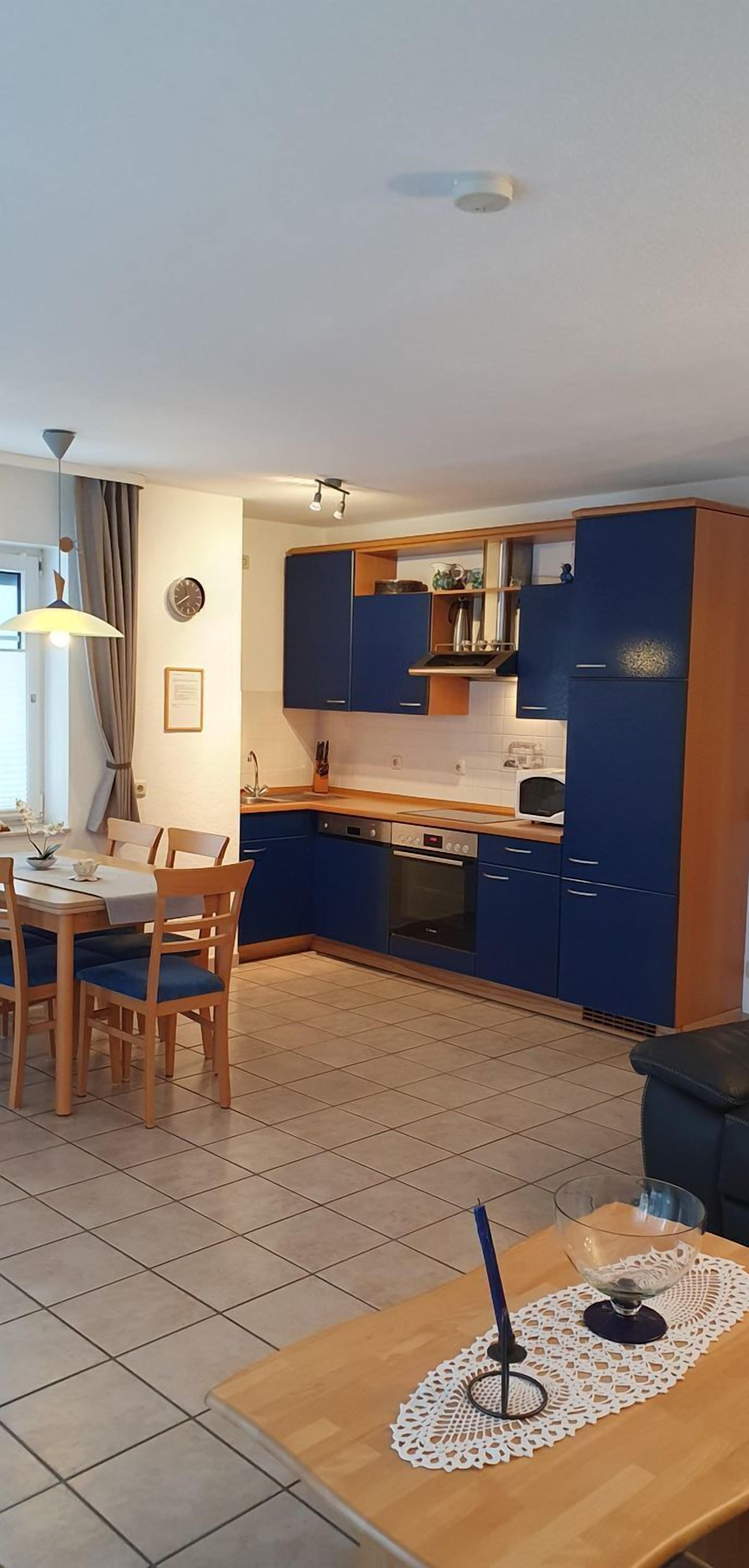 Ett modernt kök med blå skåp, en matplats med ett bord och stolar samt ett litet bord med en glasskål och ett ljus.