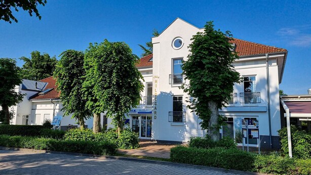 A white building with a red-tiled roof, surrounded by greenery.