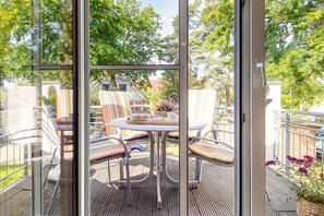 Eine Terrasse mit einem runden Tisch und gestreiften Stühlen, mit Blick auf einen Garten mit Bäumen und einem Haus im Hintergrund.
