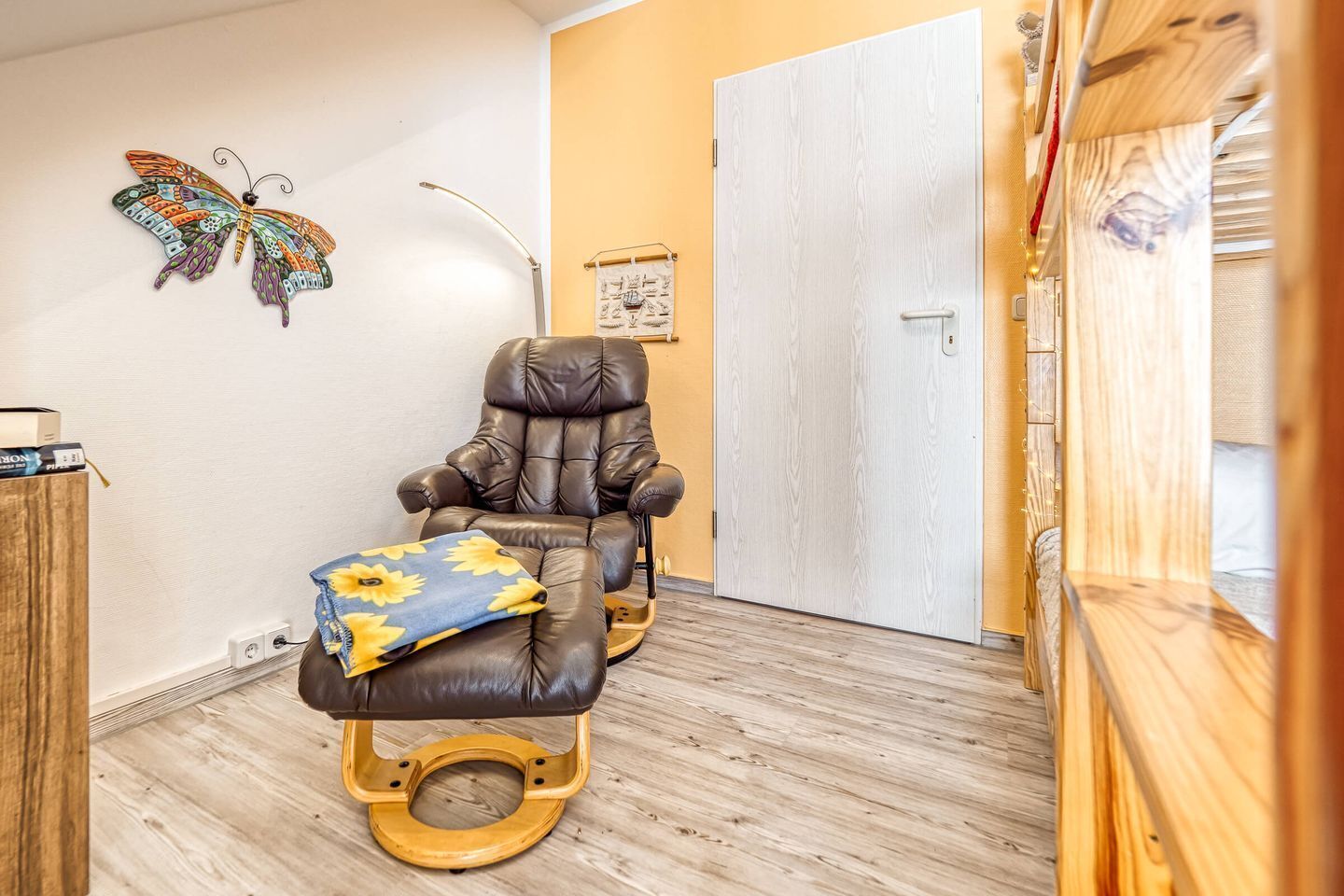 A room with a massage chair, a wooden floor, a white door, and a butterfly decoration on the wall.