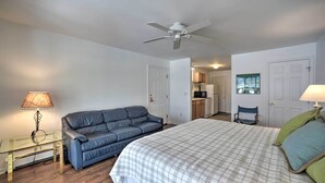 A bedroom with a bed, a blue sofa, a glass table, and a ceiling fan. - Bolton Landing Suite w/ Deck, Lake George Access (Bolton Landing)
