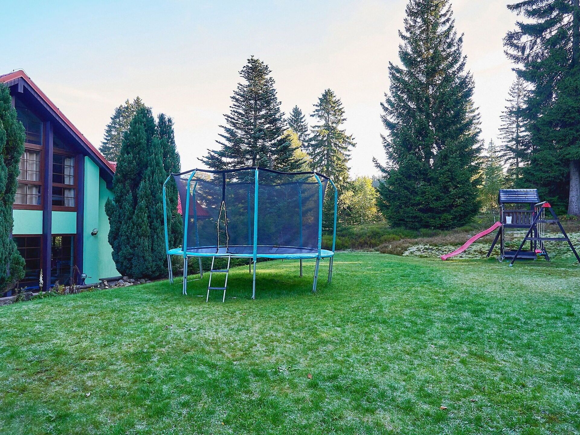 Un trampoline dans un jardin, avec une maison et des arbres.