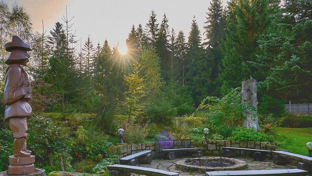 A stone fountain surrounded by stone benches in a lush garden with trees and a wooden sculpture. - Beautiful private villa for 14 guests with WIFI, private pool, TV, terrace and panoramic view (Jablonec Nad Nisou)