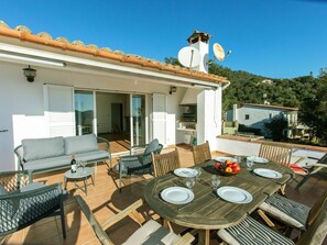 Une terrasse extérieure avec une table à manger pour quatre personnes, entourée de chaises en osier et d’un canapé.