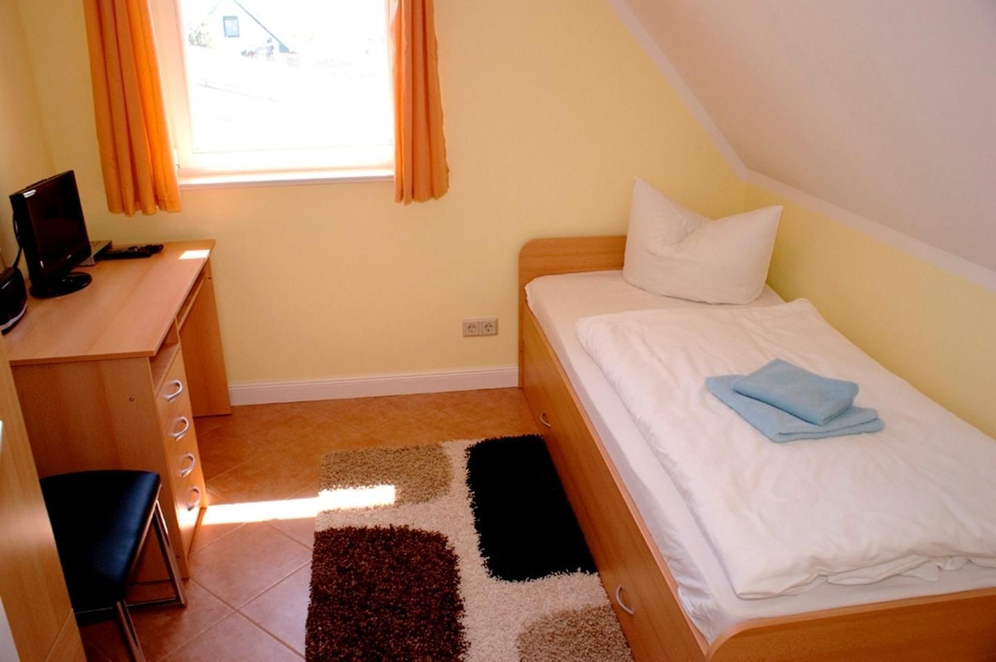 A bedroom with a bed, a desk, a chair, and a window with curtains.