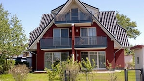 Un immeuble résidentiel à deux étages, doté d’une façade rouge, de grandes fenêtres et d’un balcon à l’étage supérieur.