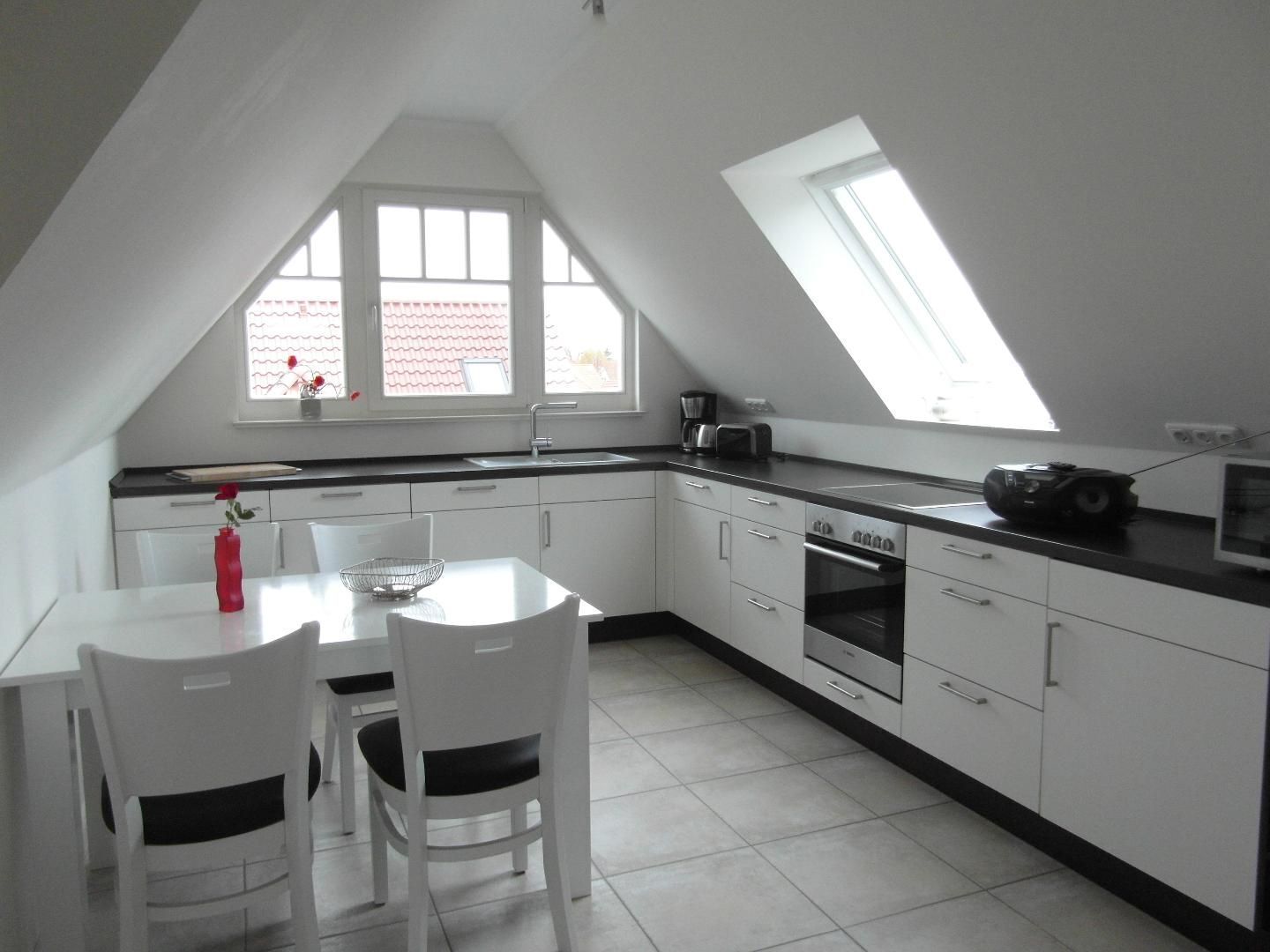 A modern kitchen with white cabinetry, a dining table with chairs, a built-in oven, and a skylight.