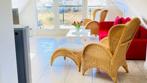 Un salon moderne avec un canapé rouge, des fauteuils en osier et une petite table blanche sur laquelle est posé un vase de fleurs.