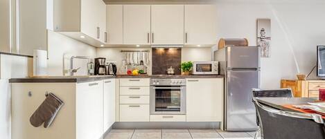 A modern kitchen with white cabinets, a built-in oven, a microwave, and a refrigerator.