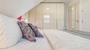 A bedroom with a bed, pillows, a wardrobe, a mirror, and a bedside table.