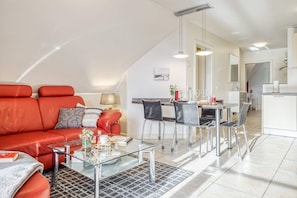 A modern apartment with a red leather sofa, a glass coffee table, and a dining area with metal chairs. - Comfortable Boddenstern vacation apartment in Zingst with balcony and WLAN - (Zingst)