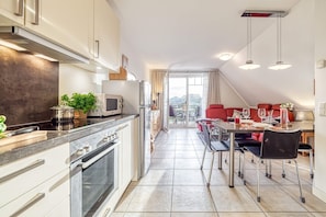 A modern kitchen with a dining area, a large window, and a red sofa. - Comfortable Boddenstern vacation apartment in Zingst with balcony and WLAN - (Zingst)