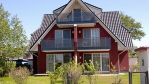 A two-story residential building with a red facade, large windows, and a balcony on the upper floor.
