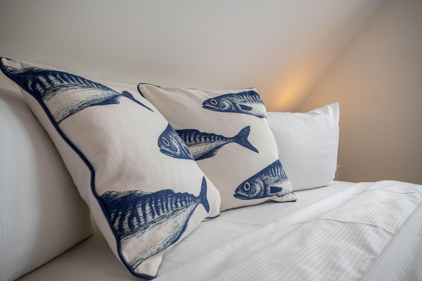 Een bed met witte beddengoed en kussens met blauwe vismotieven.