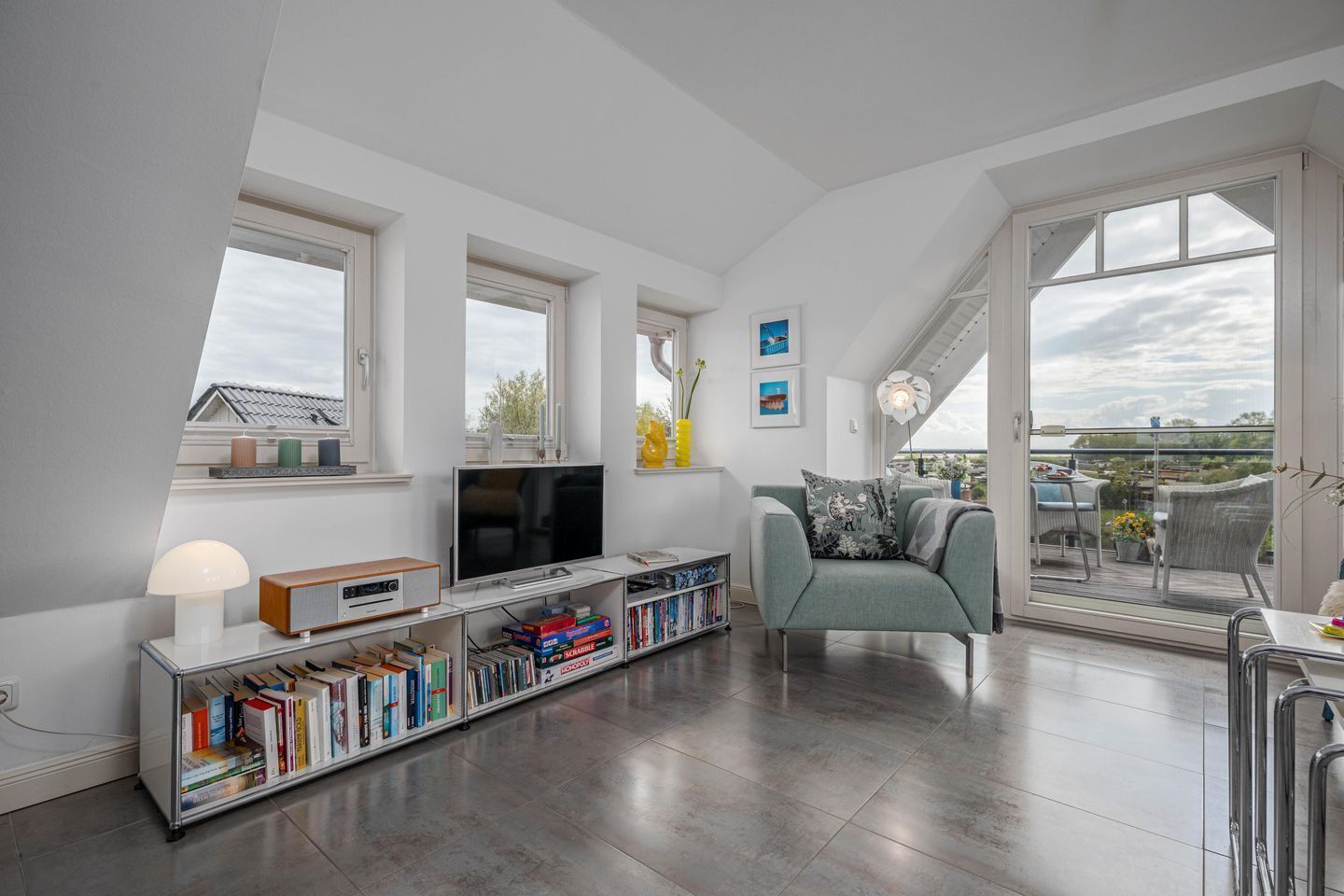 A modern living room with a flat-screen TV, bookshelves, a sofa, and a balcony with outdoor furniture.