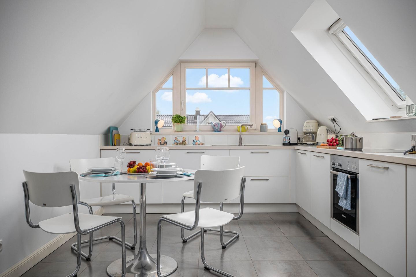 Une cuisine moderne avec un coin repas, des meubles blancs et une verrière offrant une vue sur le ciel.