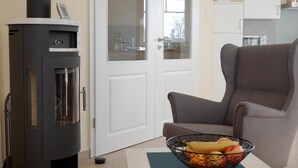 A modern living room with a black wood-burning stove, a grey armchair, and a bowl of fruit on a table. - Comfortable vacation home with terrace, wood-burning stove and modern furnishings - (Prerow)