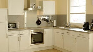 A kitchen with white cabinets, a built-in oven, a microwave, and a window providing natural light. - Comfortable vacation home with terrace, wood-burning stove and modern furnishings - (Prerow)