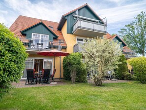 Ein zweistöckiges Haus mit einem Balkon, einer Terrasse mit Gartenmöbeln und einem gepflegten Garten.