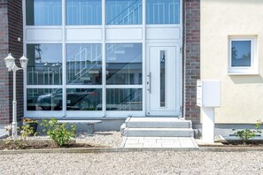Un edificio con una puerta blanca, un ventanal pequeño y una lámpara a la izquierda.