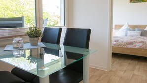 A modern room with a glass dining table, two chairs, a small potted plant, and a bed with a floral bedspread. - "Sonnenblick" in the Strandburg house... close to the beach and in a quiet location! - House (Dahme)