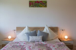 Un lit recouvert d’une courtepointe à motifs floraux, deux tables de chevet avec des lampes et un tableau accroché au mur.