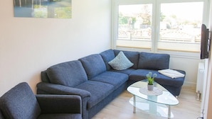 A living room with a grey sofa, a glass coffee table, and a TV mounted on the wall. - "Sonnenblick" in the Strandburg house... close to the beach and in a quiet location! - House (Dahme)