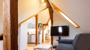 A loft-style room with a wooden beam, a flat-screen TV, a gray sofa, and a white table. - Spatzennest by Interhome (Spiez)