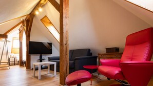 A loft-style room with a wooden ceiling, a flat-screen TV, a red chair, a small table, and a sofa. - Spatzennest by Interhome (Spiez)