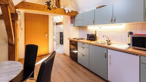A modern kitchen with wooden beams, a dining area with a marble table, and a view into the bathroom. - Spatzennest by Interhome (Spiez)