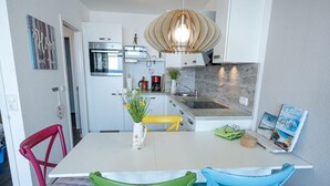 Een moderne keuken met witte kasten, een inbouwoven, een hanglamp en een eethoek met kleurrijke stoelen.