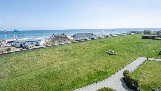Een landgoed aan de kust met een gazon, een verhard pad en een gebouw met rieten dak.