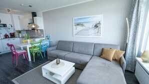 Een moderne woonkamer met een grijze bank, een witte salontafel en kleurrijke stoelen.