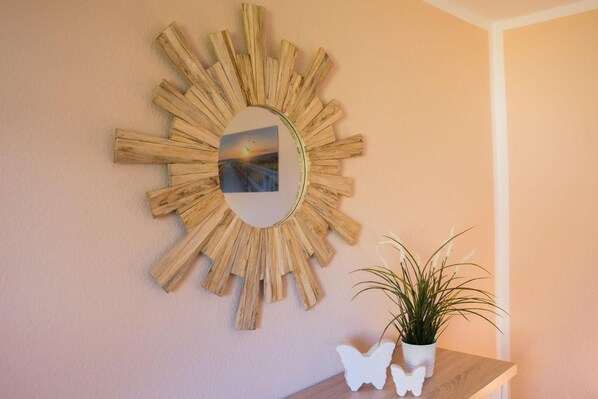 A wall-mounted sunburst mirror with a picture inside, a potted plant, and two butterfly-shaped objects on a wooden table.