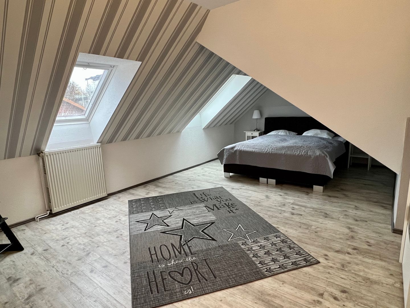 A bedroom with a sloped ceiling, a bed, a nightstand, a lamp, and a star-patterned rug.