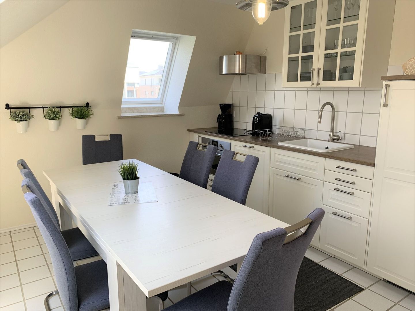 Una cocina moderna con comedor, armarios blancos, una ventana y una cafetera.