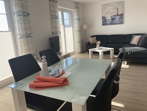 Un comedor con una mesa de vidrio, sillas negras y una pequeña mesa blanca con una lámpara.