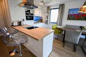 Eine moderne Küche mit Kochinsel, Barhocker, Essbereich mit Tisch und Stühlen sowie einem großen Fenster mit Vorhängen.