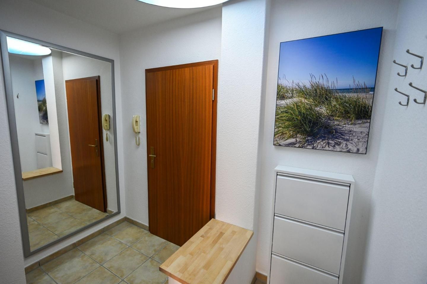 A hallway with a wooden door, a mirror, a telephone, a small table, a cabinet, and a beach-themed picture on the wall.