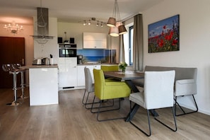 Eine moderne Küche mit weißen Schränken, ein Essbereich mit einem Holztisch und Stühlen sowie ein Blumenbild an der Wand.