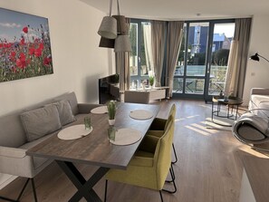 Ein modernes Wohnzimmer mit Essbereich, einer Couch, einem Couchtisch und einem großen Fenster mit Vorhängen.