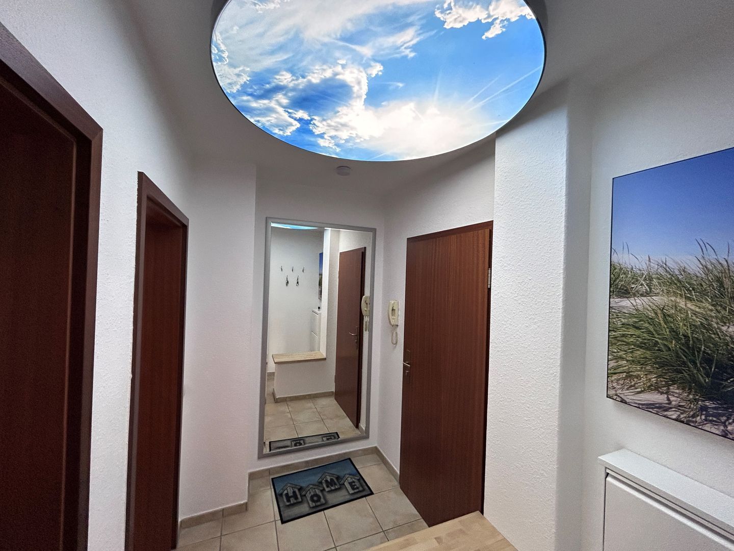A hallway with a skylight, wooden doors, a bathroom visible through the glass, and a doormat with 'HOME' on it.