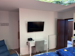 Ein Schlafzimmer mit Bett, Schreibtisch mit Stuhl, einem an der Wand montierten Fernseher und einem Kleiderschrank.