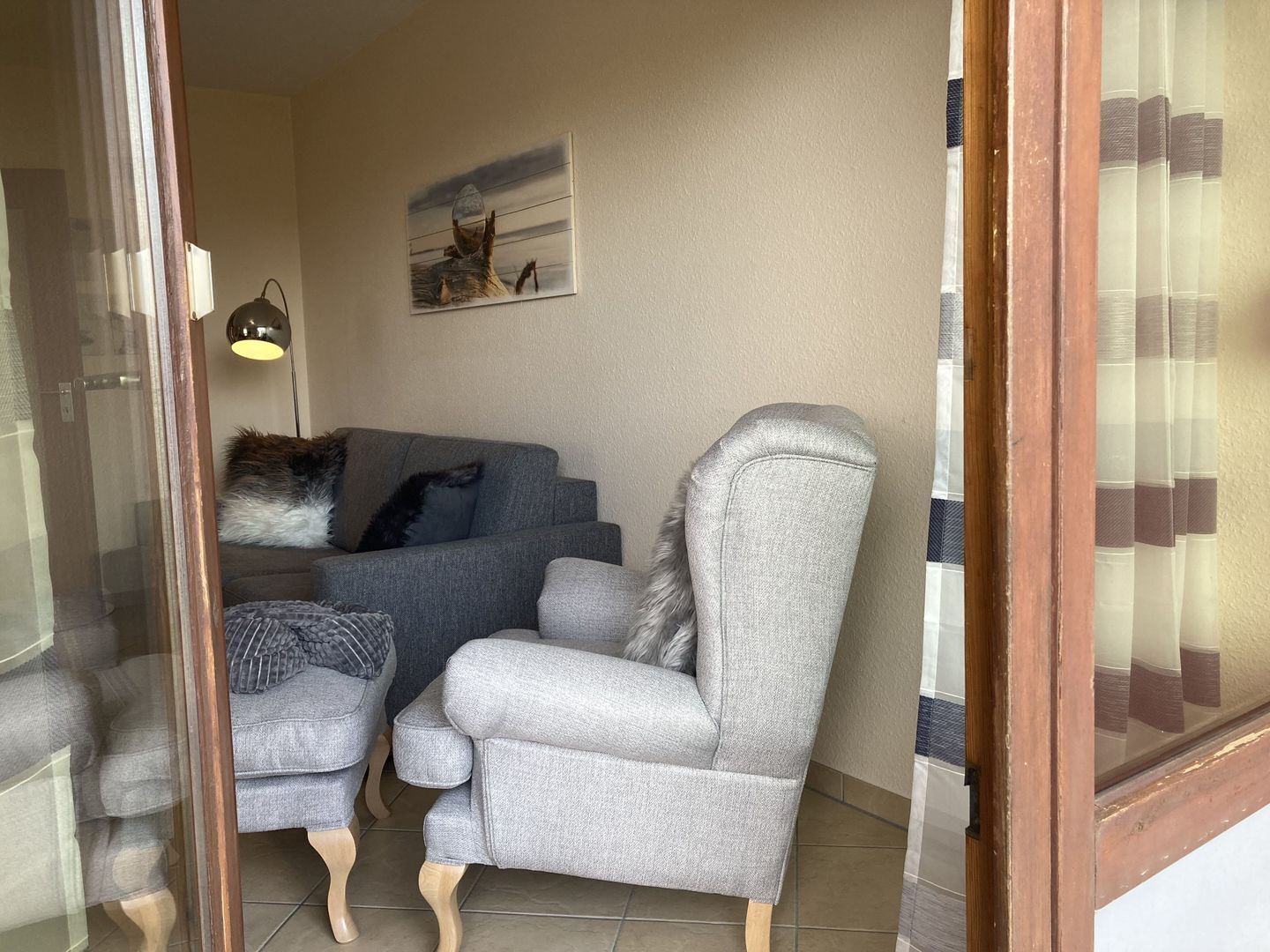 A living room with a grey sofa, a grey armchair, and a small table with a lamp.