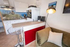 Uma cozinha compacta com bancada de madeira, parede com detalhe vermelho, um banco de bar e uma luminária pendente moderna.