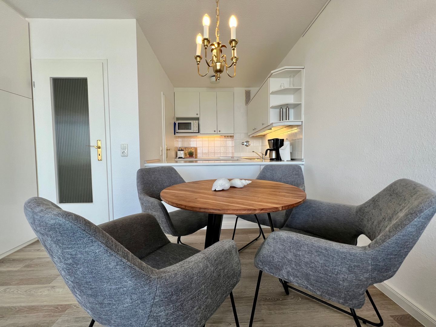 A modern kitchen with white cabinets, a microwave, and a coffee maker. There is a round wooden table with two grey chairs.