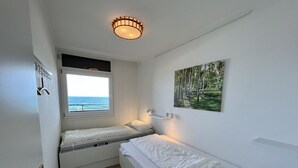 A small, clean room with two beds, a window with a view of the sea, and a painting on the wall. - Beach hotel - 56 - sea view and beach chair included! (Dahme)