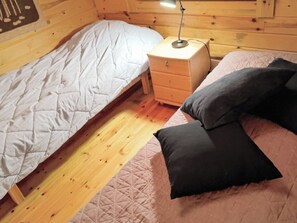 A single bed with a quilted cover, a bedside table with a lamp, and a wooden floor.