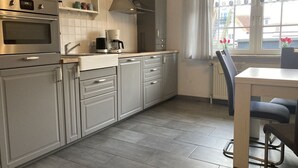 Ett modernt kök med gråa skåp, en inbyggd ugn, en kaffebryggare och ett fönster med gardiner.