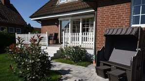 Ett hus byggt av tegel med en uteplats, ett vitt staket och en plats för grillning.
